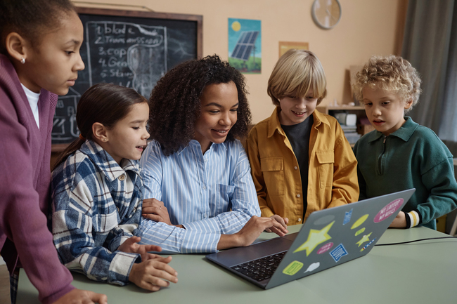 A young teacher teaches her elementary students using a laptop